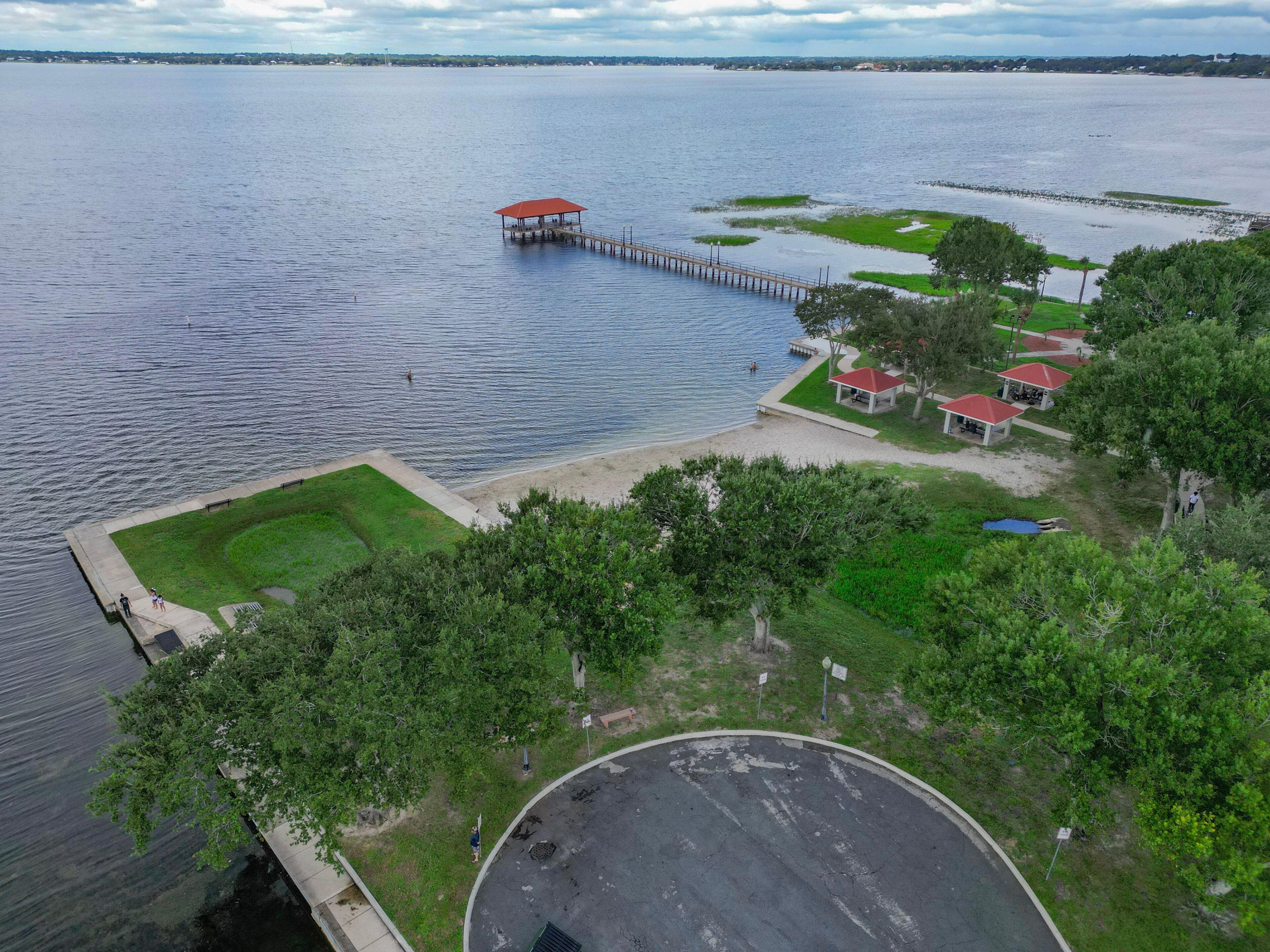 Vista para o lago com um cais, um pequeno píer e uma área gramada com construções de telhado vermelho.