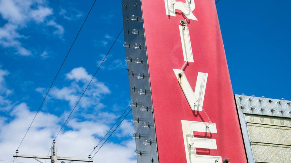 A red sign with the word "DRIVEN" on a pole against a blue sky.
