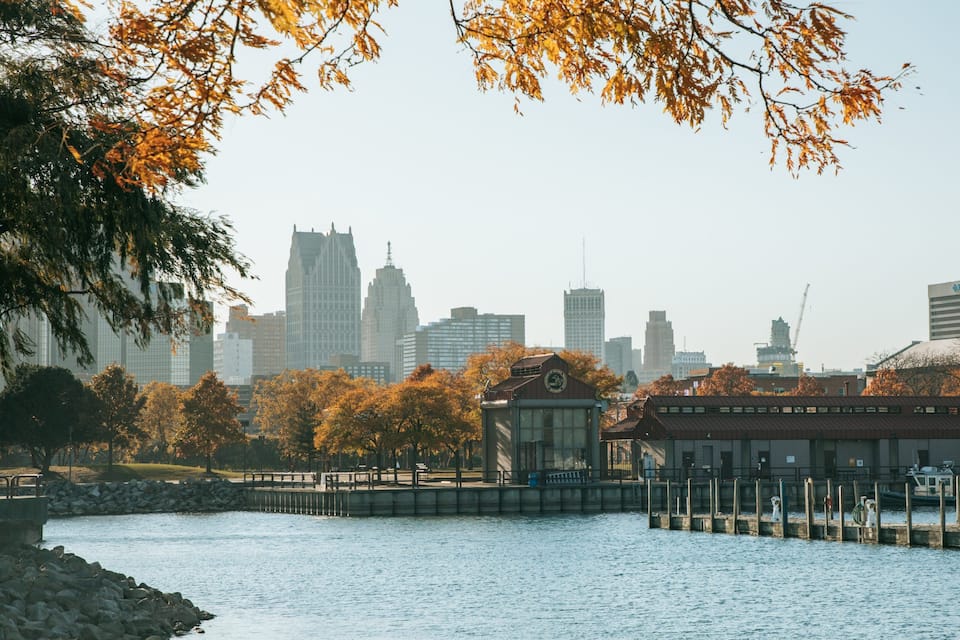A riverside cityscape with autumn foliage, a bridge, and modern buildings.