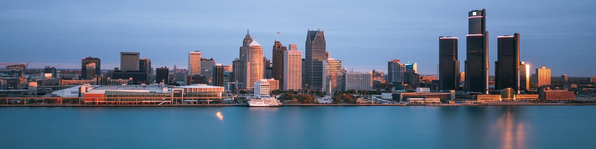 A city skyline with tall buildings and a calm body of water in the foreground.