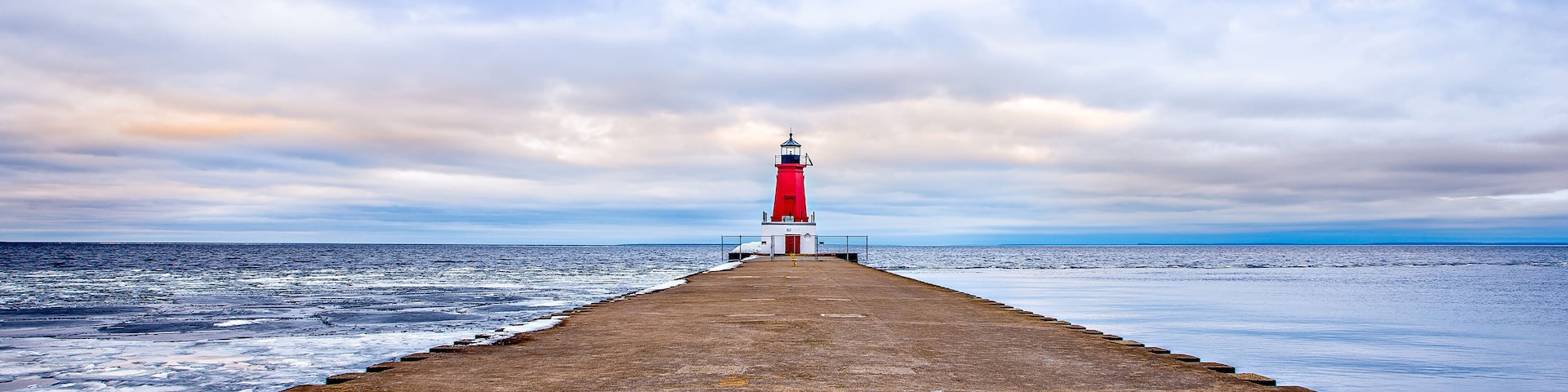 A lighthouse on a pier extending into the sea under a cloudy sky.