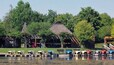 Une zone au bord du lac, avec un bâtiment à toit de chaume, des bateaux et une végétation luxuriante.