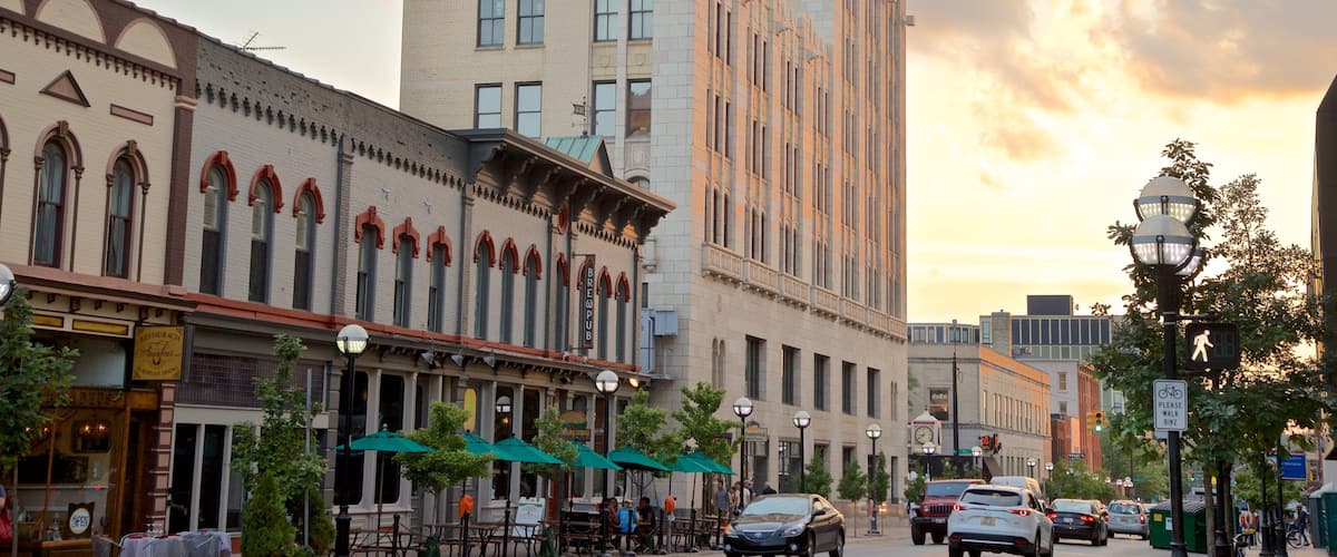 A street with historic buildings, outdoor seating, and cars.