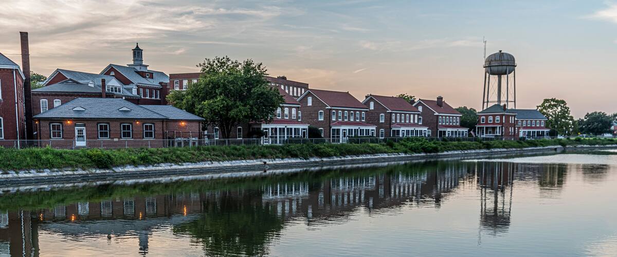 A calm river reflecting buildings and a water tower.