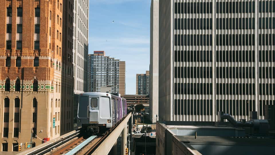 A train on elevated tracks in an urban setting with tall buildings.
