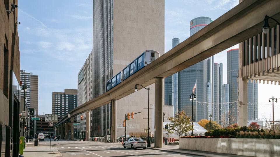 A city street with a train on an elevated track, tall buildings, and a street sign for Woodward.