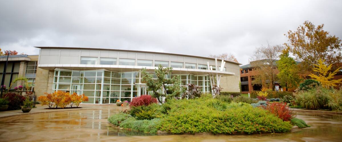 A modern building with large glass windows, surrounded by a well-maintained garden with various shrubs and trees.