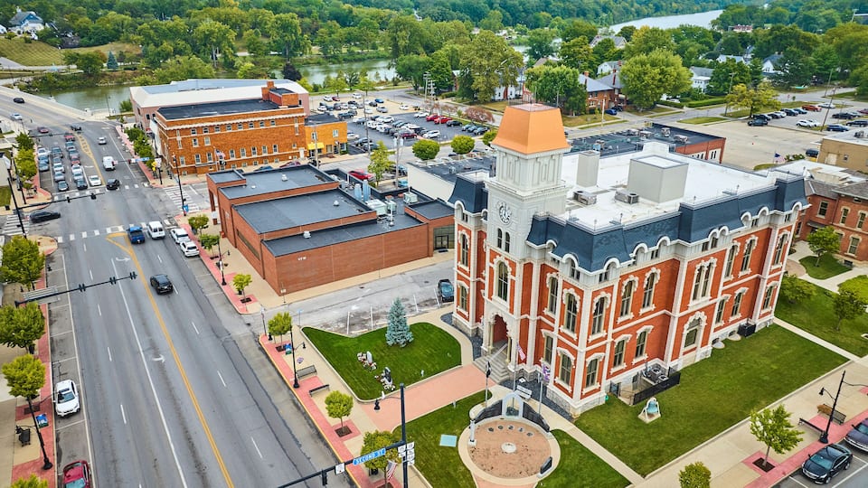 A town square with a historic building, a parking lot, and a river in the background.