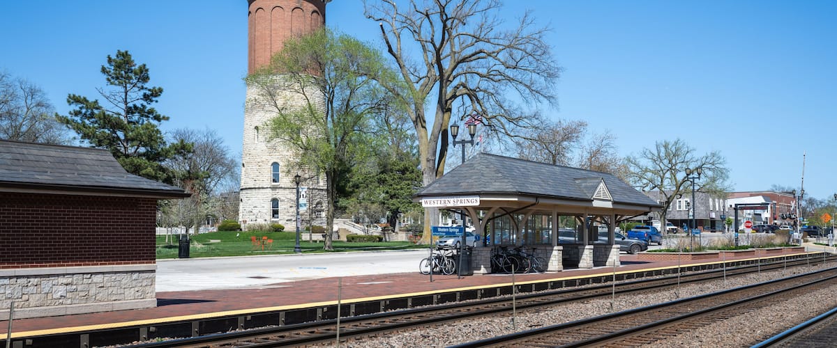 A train station with a brick building, a covered waiting area, and a tower.