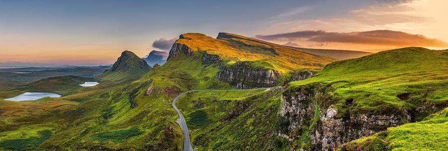 Un camino sinuoso que atraviesa un paisaje montañoso con colinas verdes y acantilados rocosos.