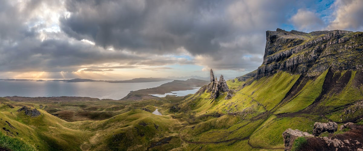 A rugged landscape with green hills, a body of water, and a cloudy sky.