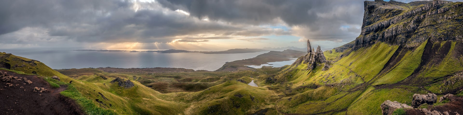 A rugged landscape with green hills, a body of water, and a cloudy sky.
