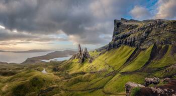 A rugged landscape with green hills, a body of water, and a cloudy sky.