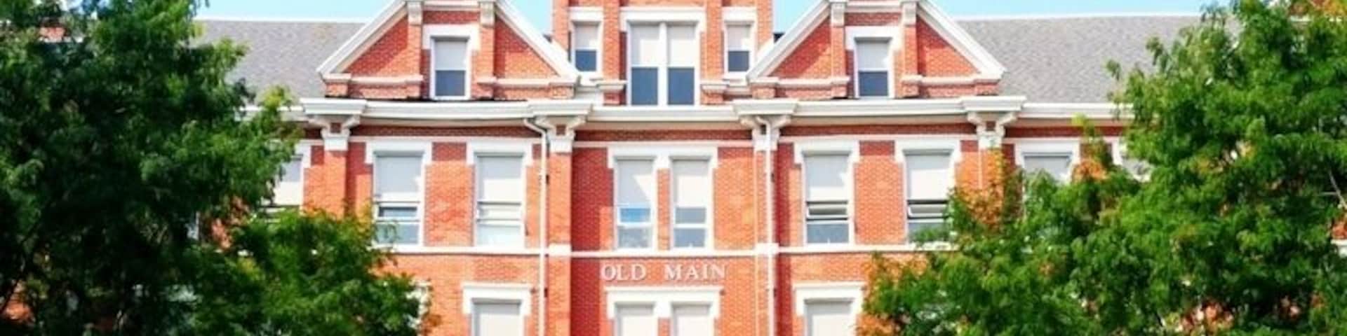 Um grande edifício de tijolos com telhado pontiagudo e uma placa que diz 'Old Main'.