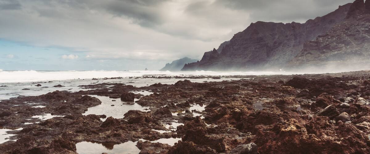 A rocky shoreline with waves crashing against the rocks under a cloudy sky.