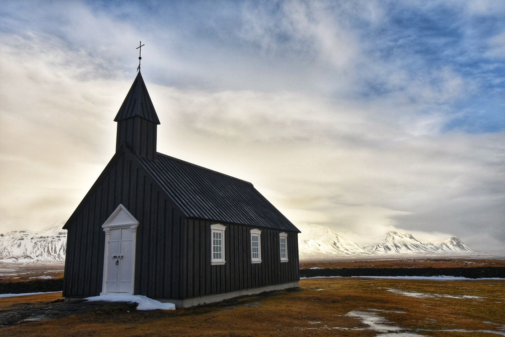 Budakirkja (The Black Church) in Iceland is a beautiful place to visit. Great to photo also. I visited Iceland in February so the mountains in the background were still full of snow which gave a great contrast against the church. #iceland #icelandtravel #parks #landscape #roadtrip #snow #winter #mountains