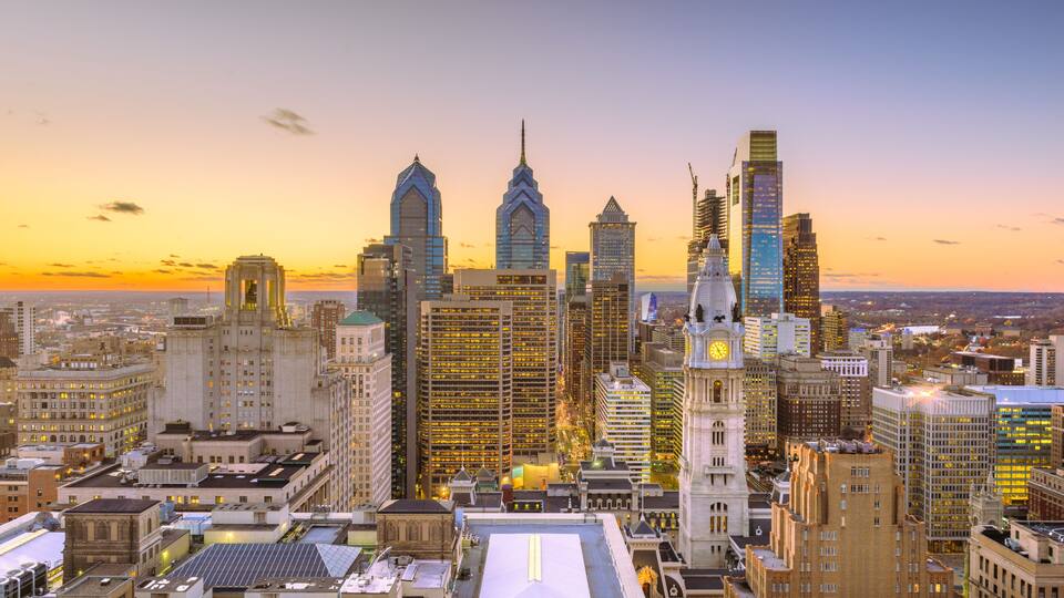 A city skyline with prominent buildings, including a clock tower and a large white-roofed structure.