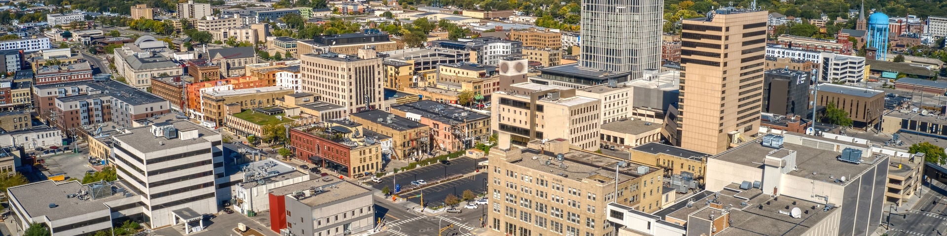 A cityscape with a mix of modern and older buildings, a prominent water tower, and a clear blue sky.