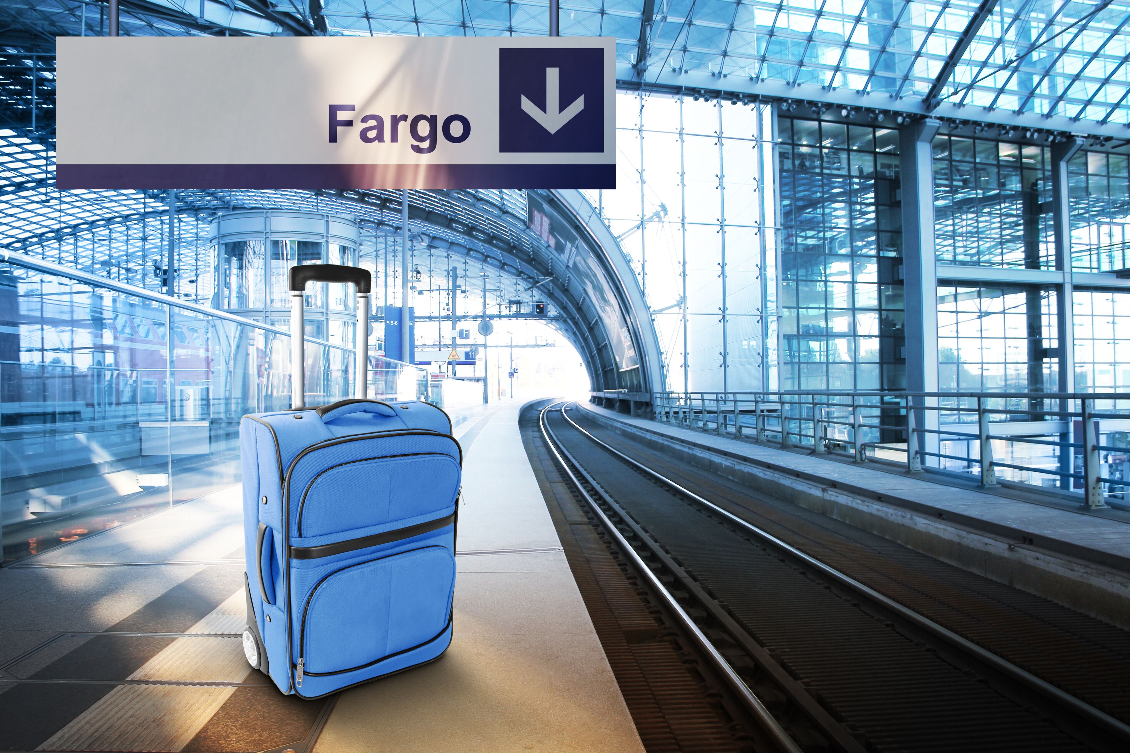 Uma mala azul em um pátio de trem, com uma placa indicando a direção para a estação Fargo.