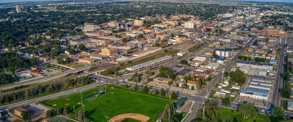 An aerial view of a city with a large green park, a baseball field, and dense urban buildings.