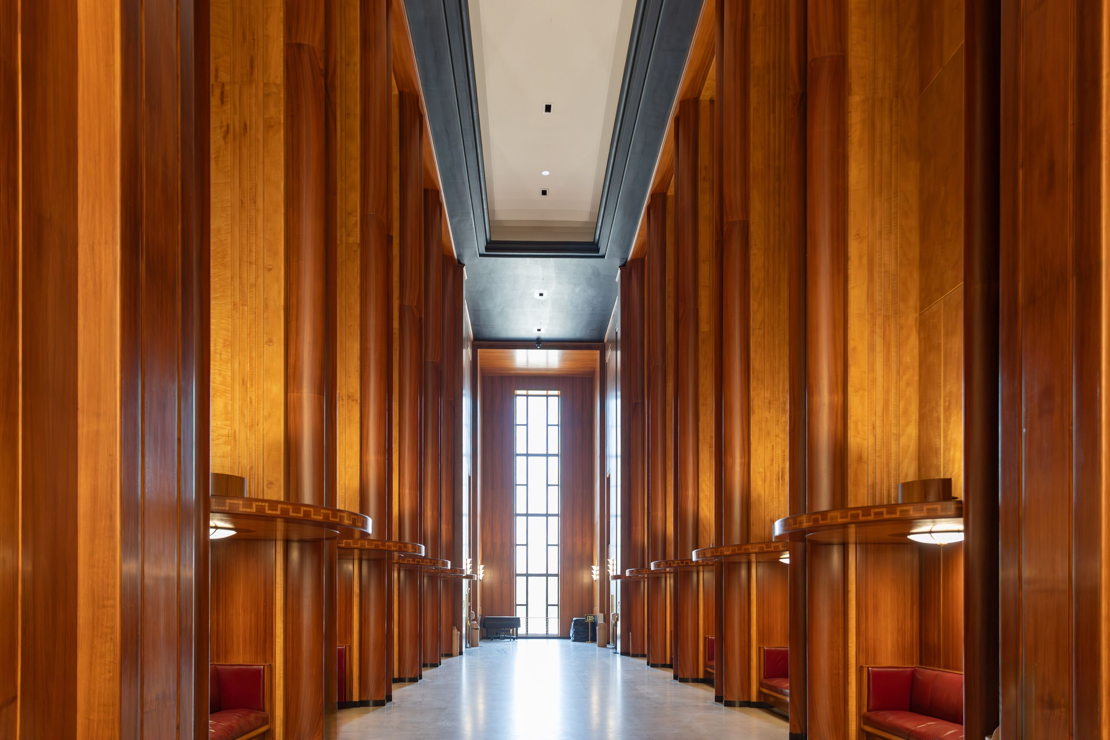 A long corridor with wooden paneling and red benches.