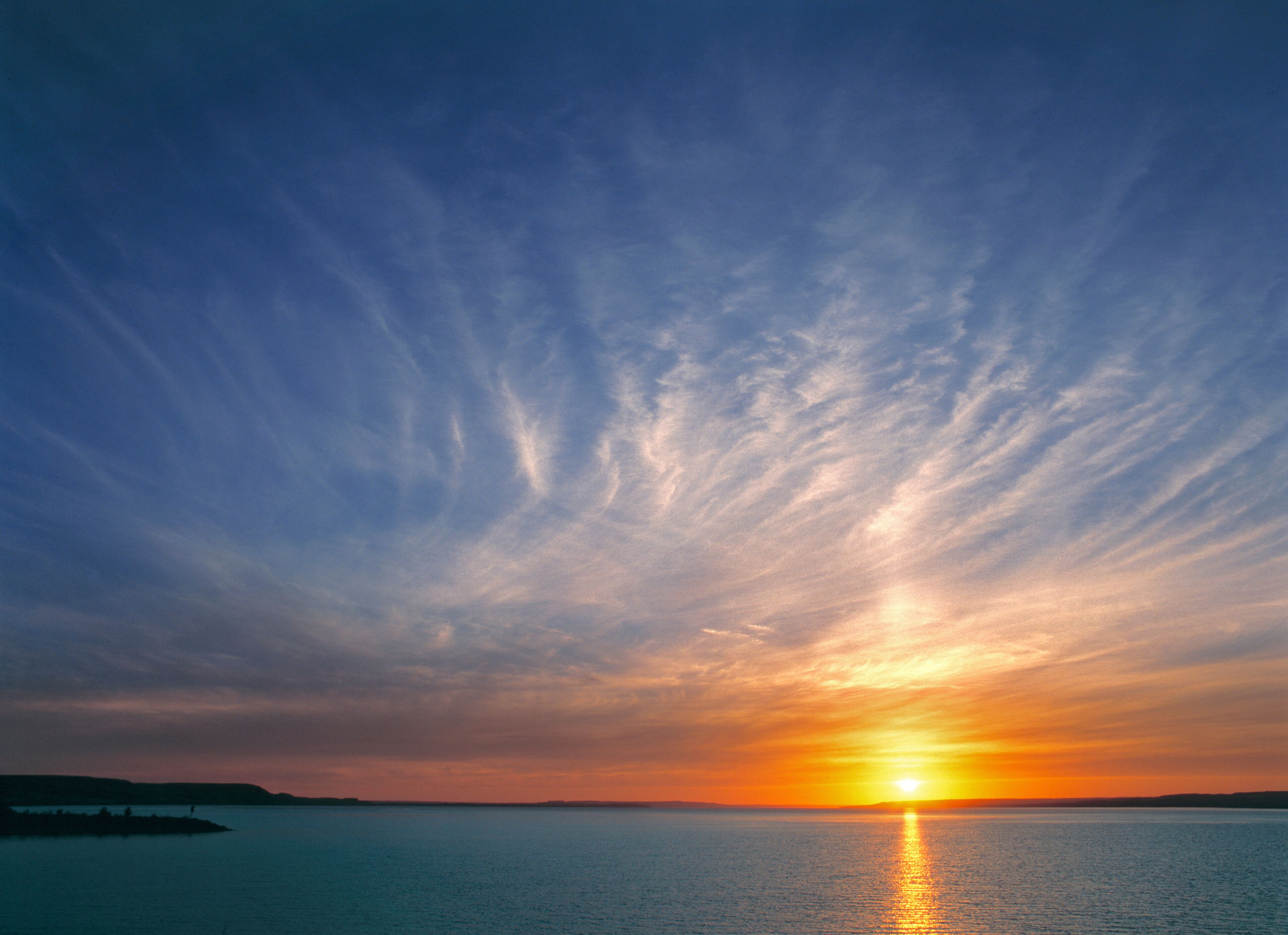 Um pôr do sol sobre um mar calmo, com céu claro e terra ao longe.