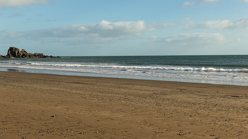 Ein sandiger Strand mit sanften Wellen, einem Felsen und einem klaren Himmel.