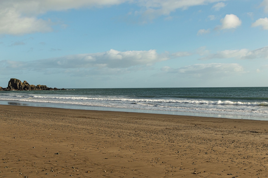 A sandy beach with gentle waves, a rocky outcrop, and a clear sky.