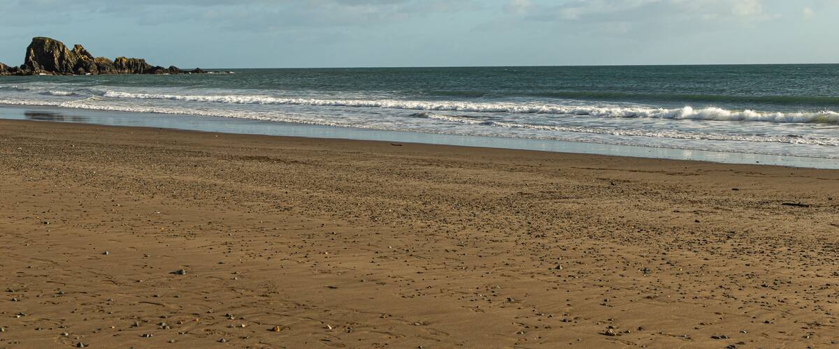 A sandy beach with gentle waves, a rocky outcrop, and a clear sky.