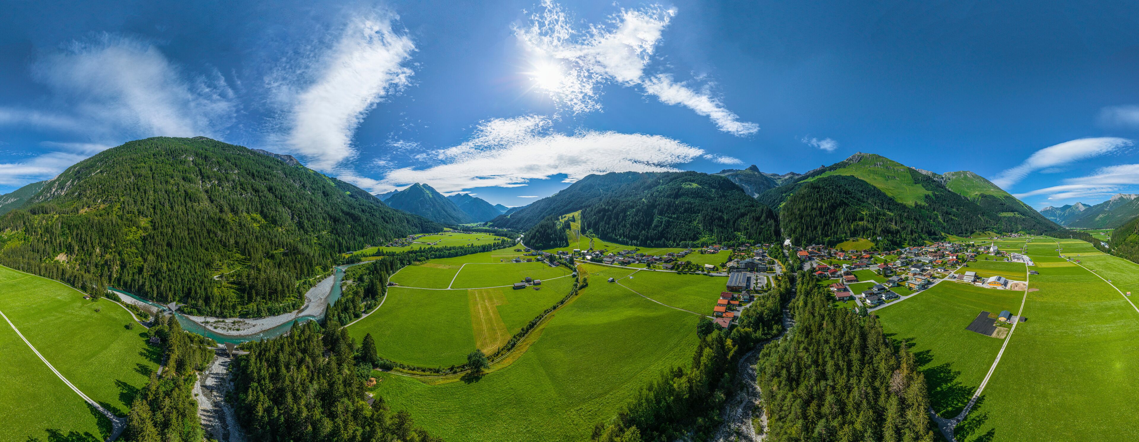 A mountainous landscape with a river, green fields, and a small village.