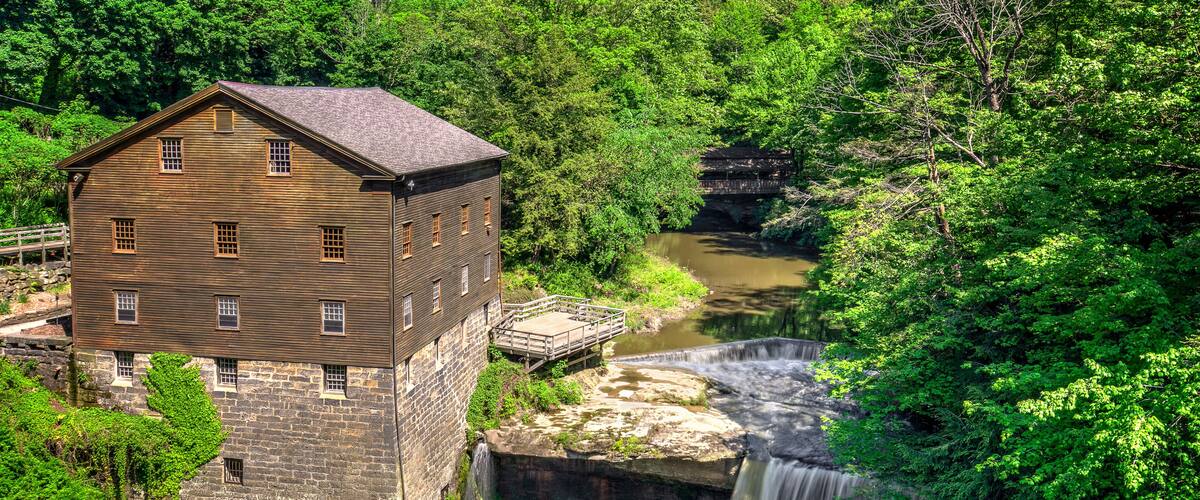 A historic stone building with a wooden structure, a waterfall, and lush greenery.
