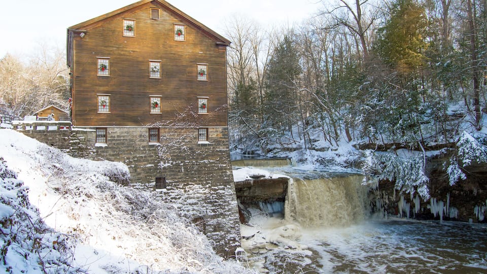 A wooden building with multiple windows, a stone base, and a waterfall in the background.