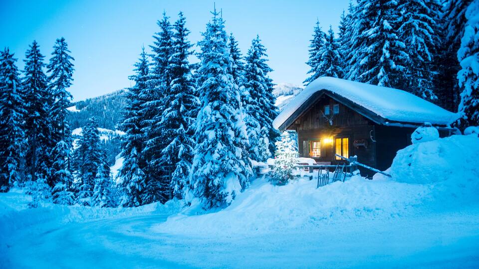 A snow-covered cabin surrounded by evergreen trees.