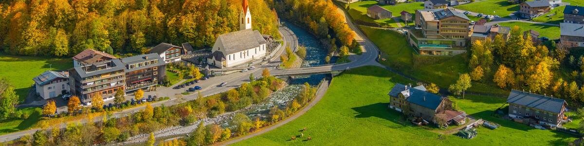 A village nestled in a valley with a river, surrounded by autumn-colored trees and mountains.