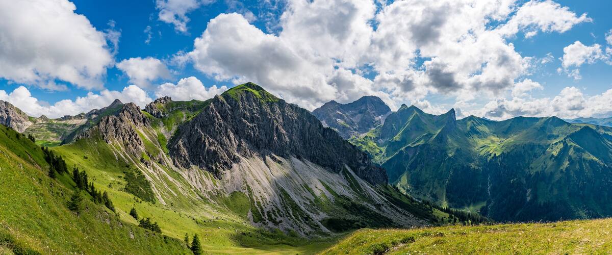 A mountainous landscape with green valleys and rocky peaks under a partly cloudy sky.