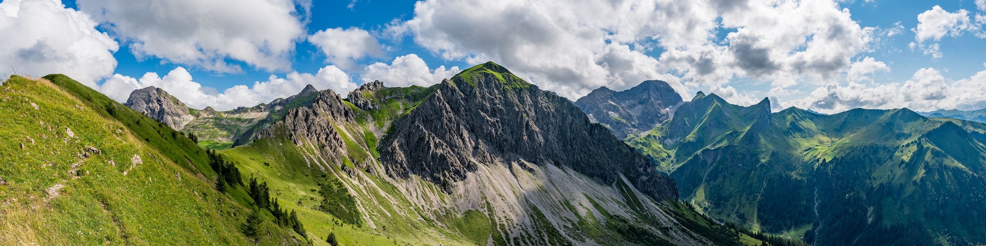 A mountainous landscape with green valleys and rocky peaks under a partly cloudy sky.