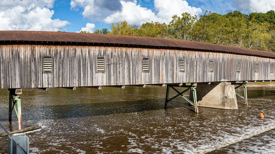 A wooden covered bridge over a river with a metal walkway on the side.