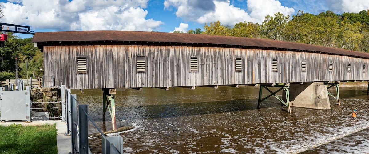 A wooden covered bridge over a river with a metal walkway on the side.