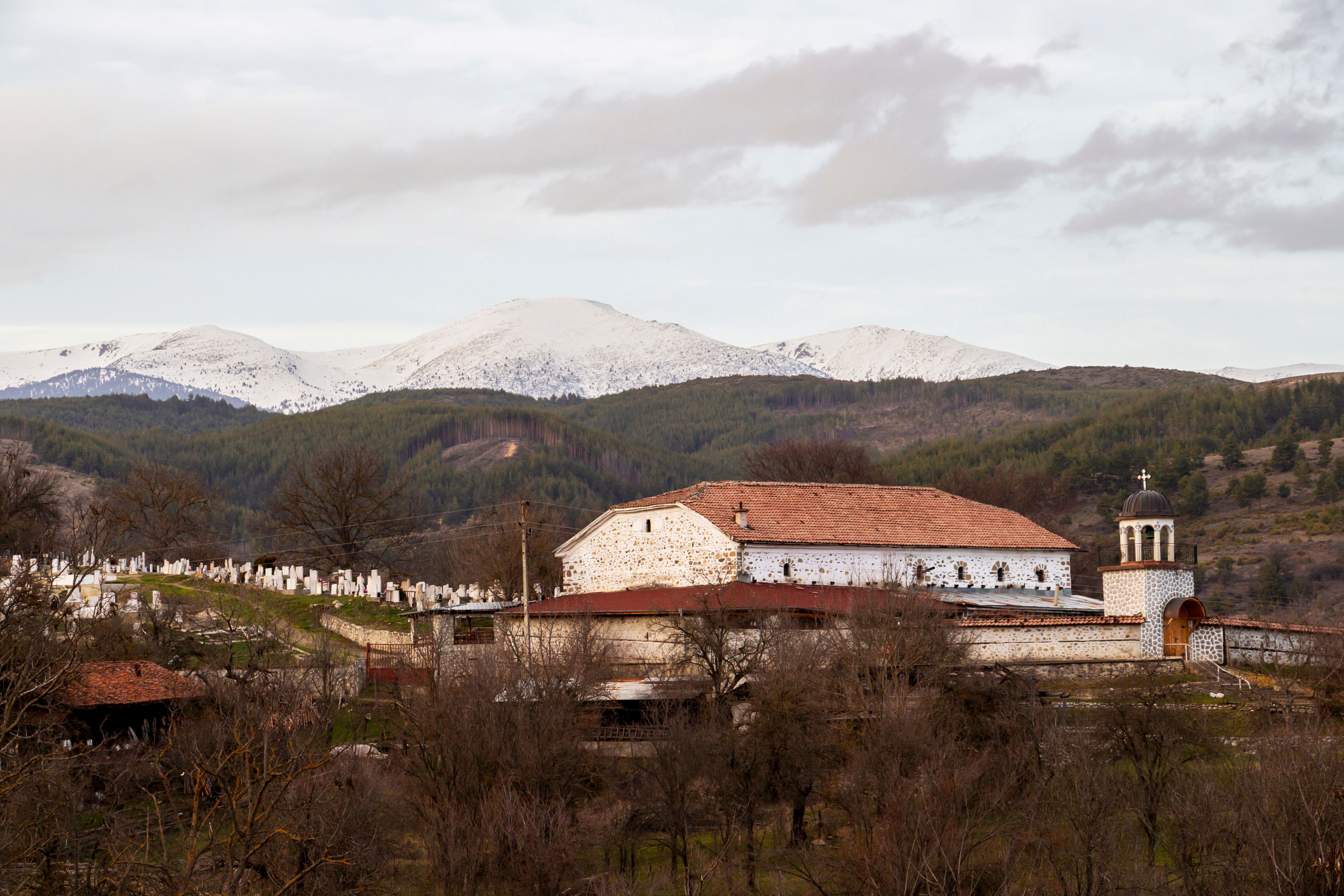 View of the Eastern Orthodox Church of the village of Gorno Draglishte from 1835, in Razlog Municipality, Blagoevgrad Province, Bulgaria, the snowy Rila Mountains in the background