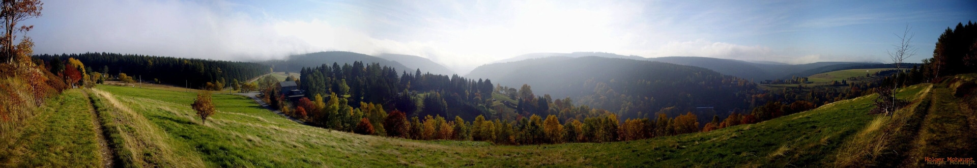 A valley with rolling hills, a winding path, and a forested area with autumn-colored trees.