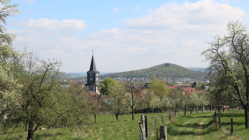 Ein Kirchturm, ein Hügel und eine Stadt im Hintergrund.