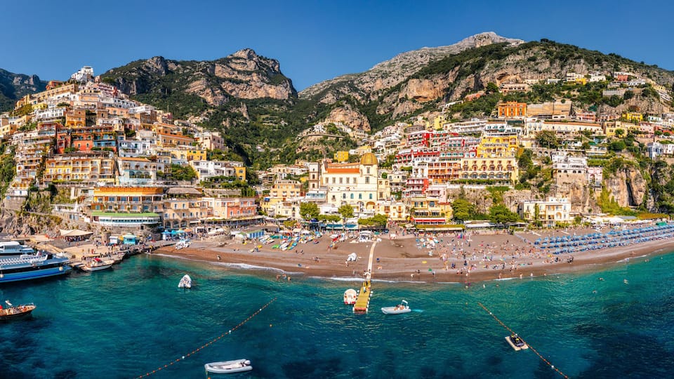 A coastal town with colorful buildings, a beach, and boats in the water.