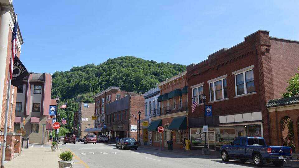 A street lined with brick buildings, a mountain in the background, and a blue pickup truck parked on the side.