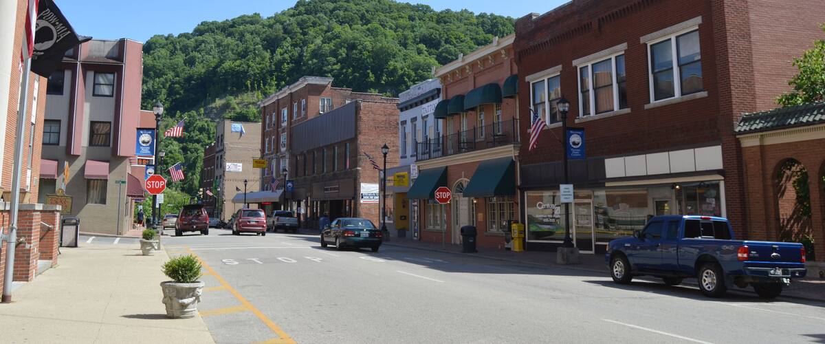 A street lined with brick buildings, a mountain in the background, and a blue pickup truck parked on the side.