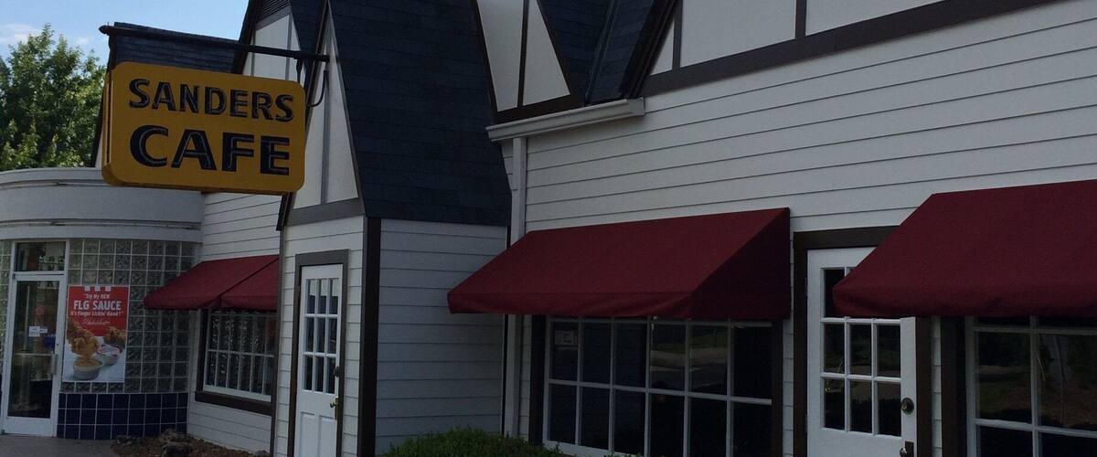 A building with a 'SANDERS CAFE' sign, red awnings, and a white door.