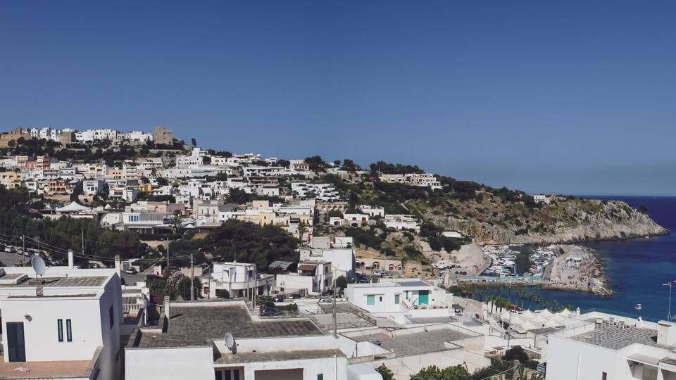 A coastal town with white buildings, a rocky hillside, and a marina with boats.