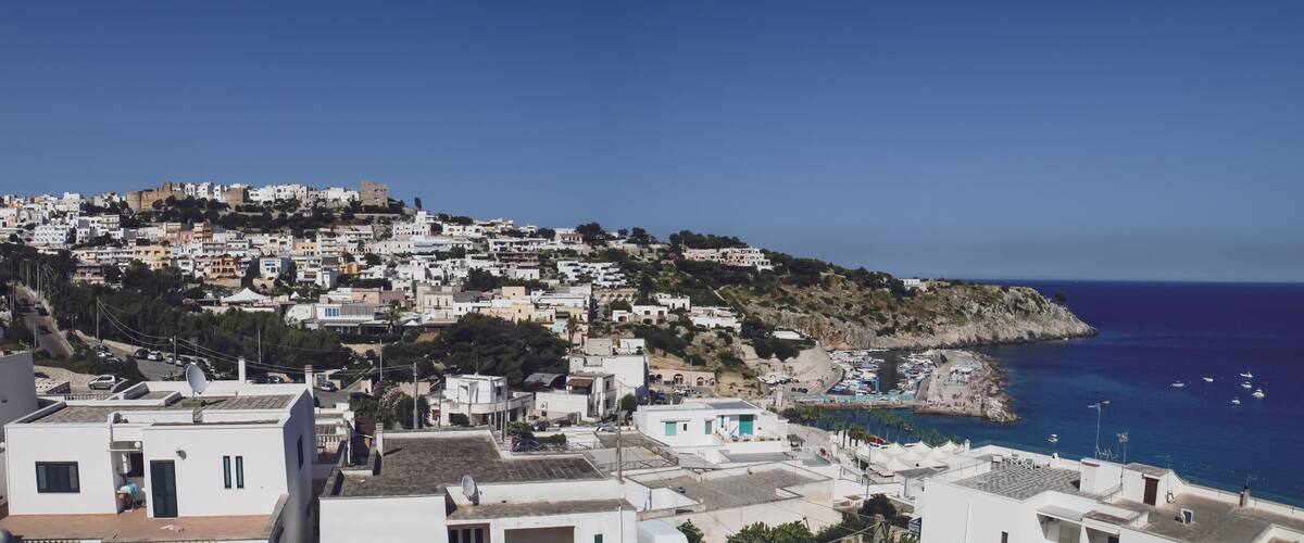A coastal town with white buildings, a rocky hillside, and a marina with boats.
