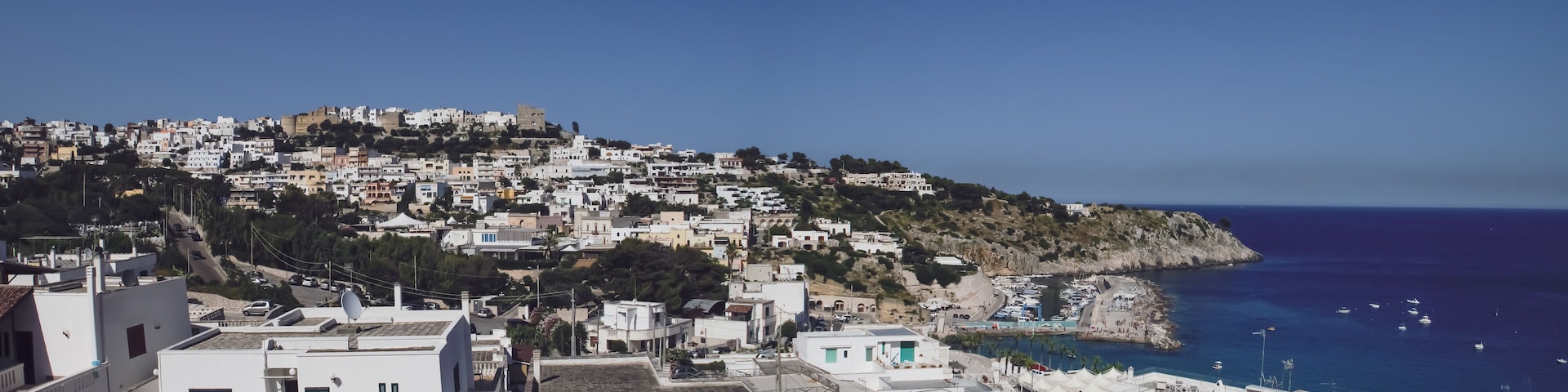 A coastal town with white buildings, a rocky hillside, and a marina with boats.