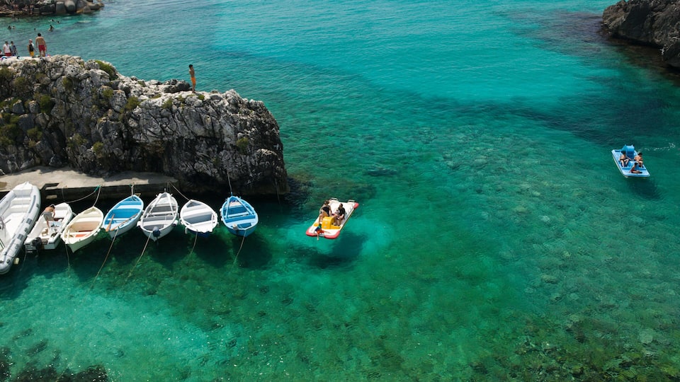 A clear turquoise sea with boats anchored near rocky cliffs.
