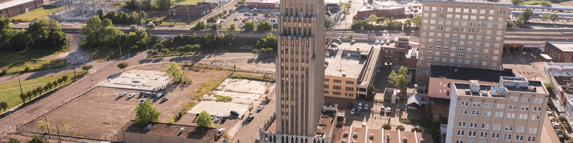 An aerial view of a cityscape with a prominent tall building with a unique design, surrounded by other buildings and a mix of urban and green spaces.